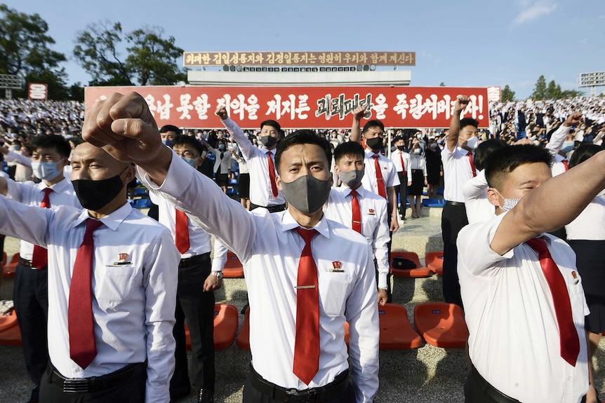 A group of young men in white shirts, red ties and face masks holding their fists up