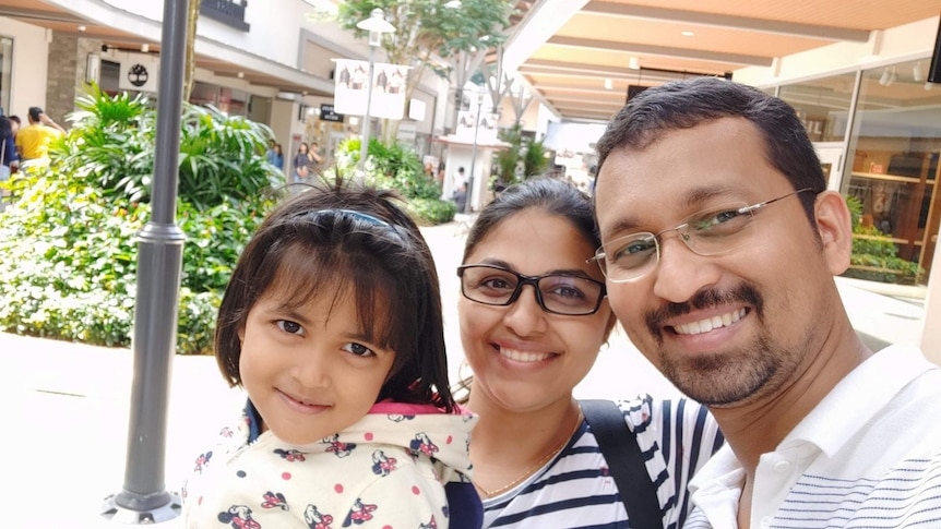 A man and woman and their daughter smile for the camera