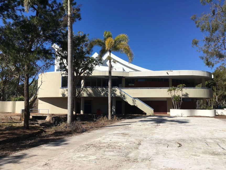 A large cement building, with plant overgrowth in the foreground across walkways