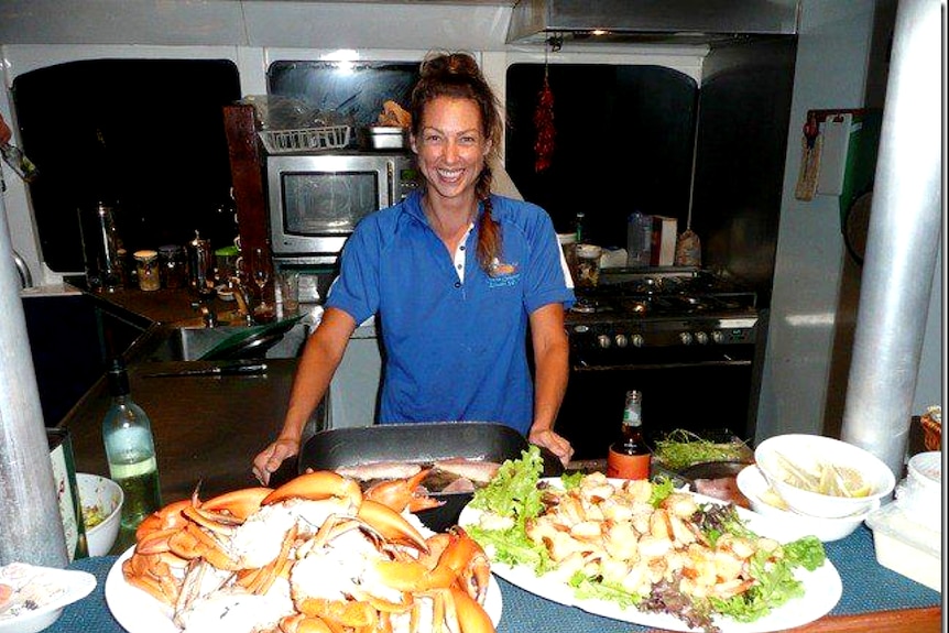 a smiling woman in a small kitchen surrounded by seafood