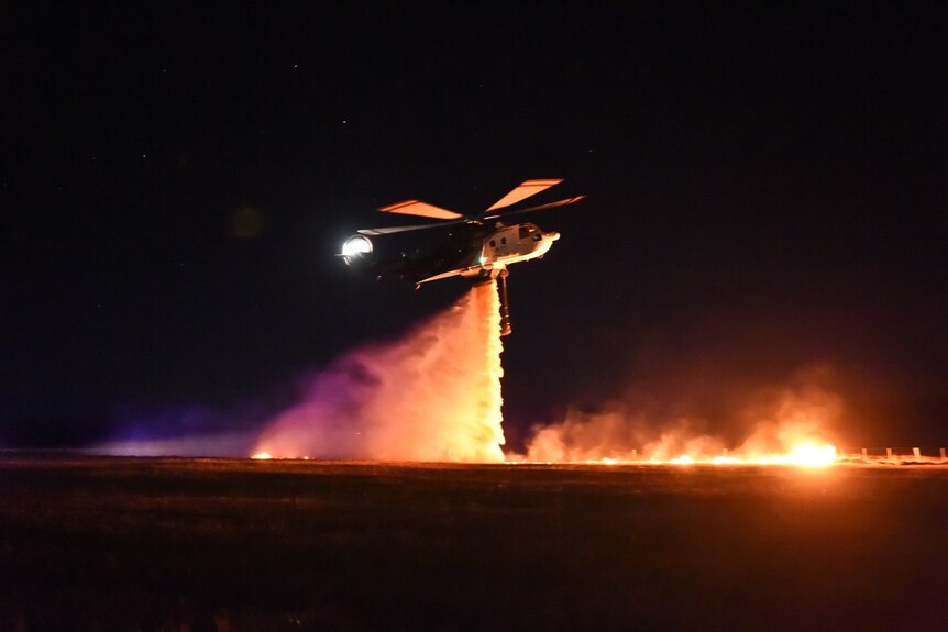 A helicopter drops water on a controlled burn during the night.