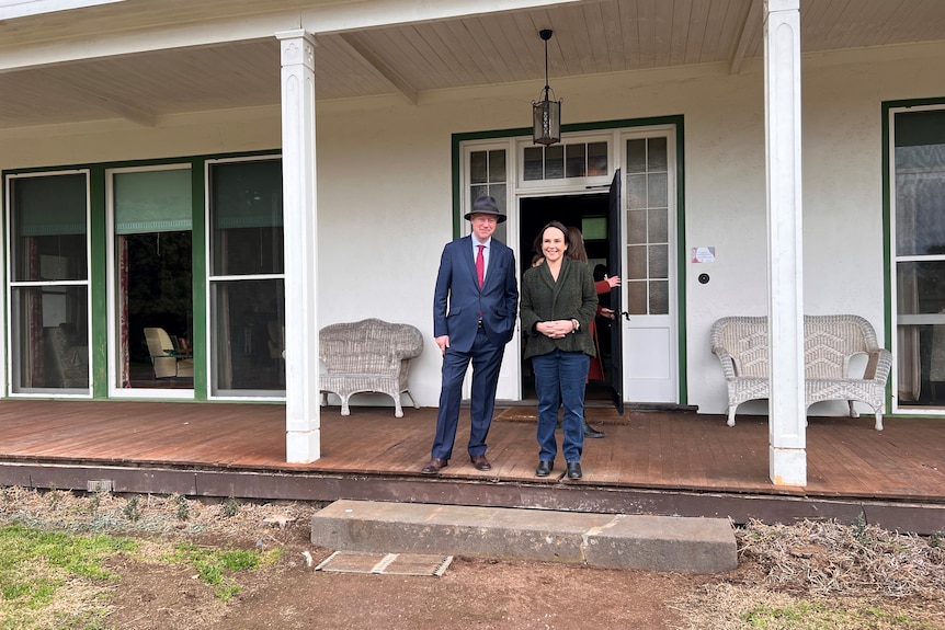 Two people grin out front of a lovely house.