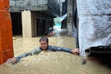 A man negotiates his way between buildings, neck-deep floodwaters in his village.