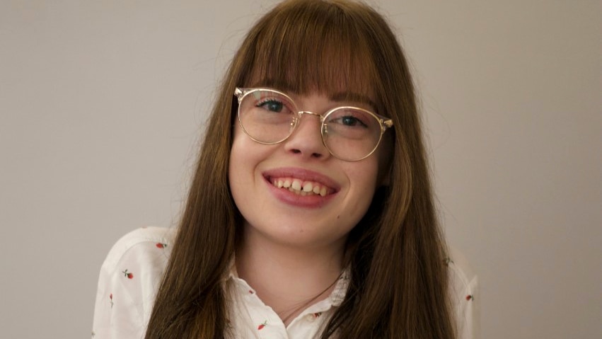 Ashleigh Gibson, who has long auburn hair and glasses, poses for a photo in a white floral shirt