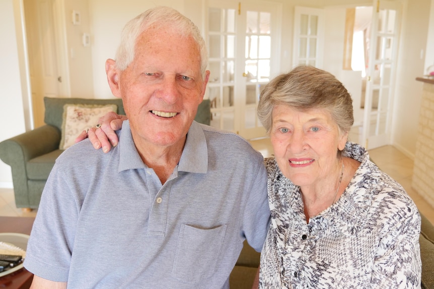 An older man with his arm around his wife in their home.