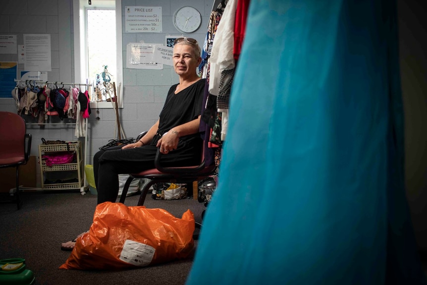 A woman with glasses on her head sits on a chair next to clothing