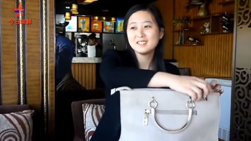 A young North Korean woman sits down with her white bag on the table. 