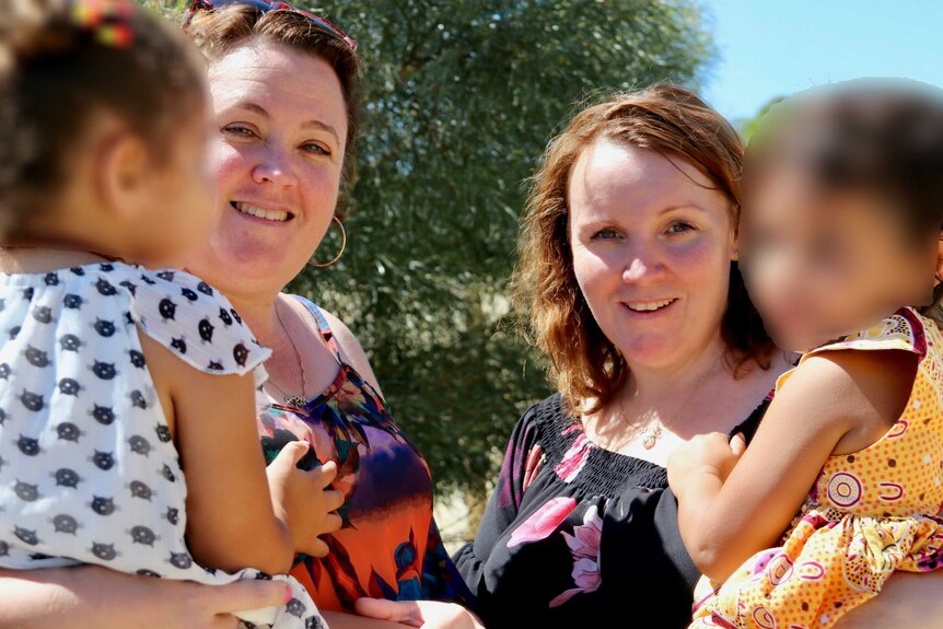 Jodie Plug and Meaghan Heath holding foster children with their faces blurred.