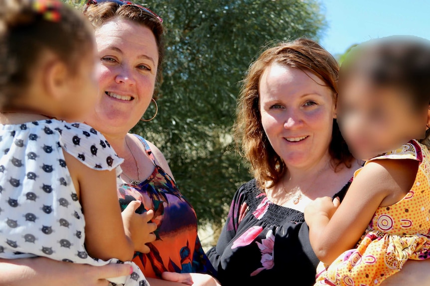 Jodie Plug and Meaghan Heath holding foster children with their faces blurred.