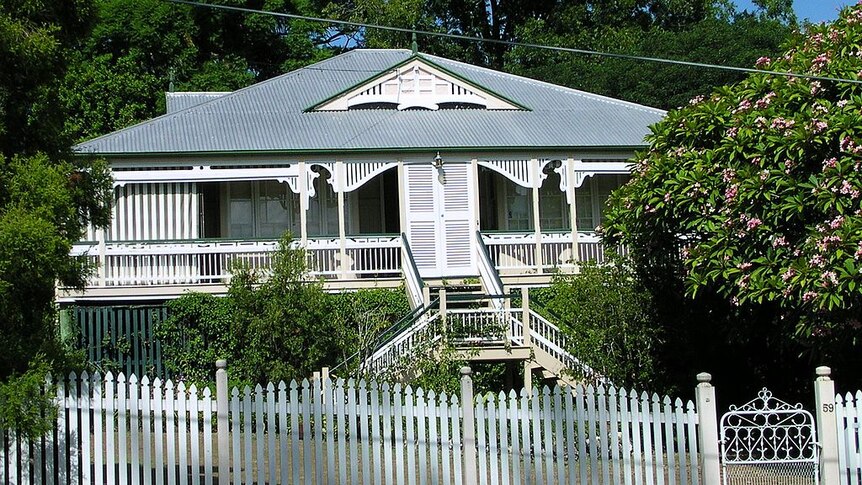 A white fenced victorian-era Queenslander photographed from street level