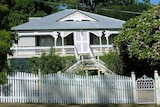 A white fenced victorian-era Queenslander photographed from street level