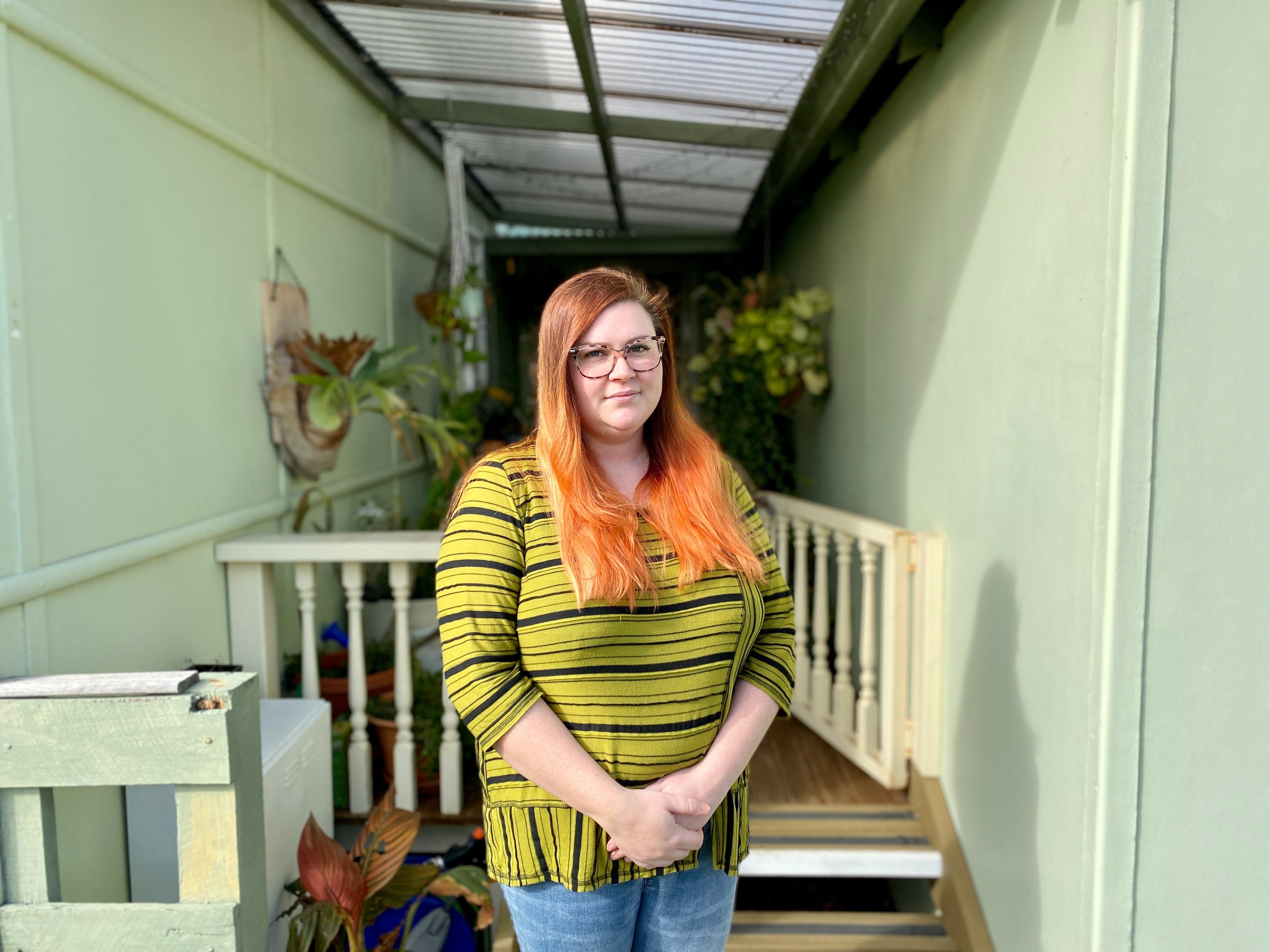 A woman with bright hair standing in front of her house.
