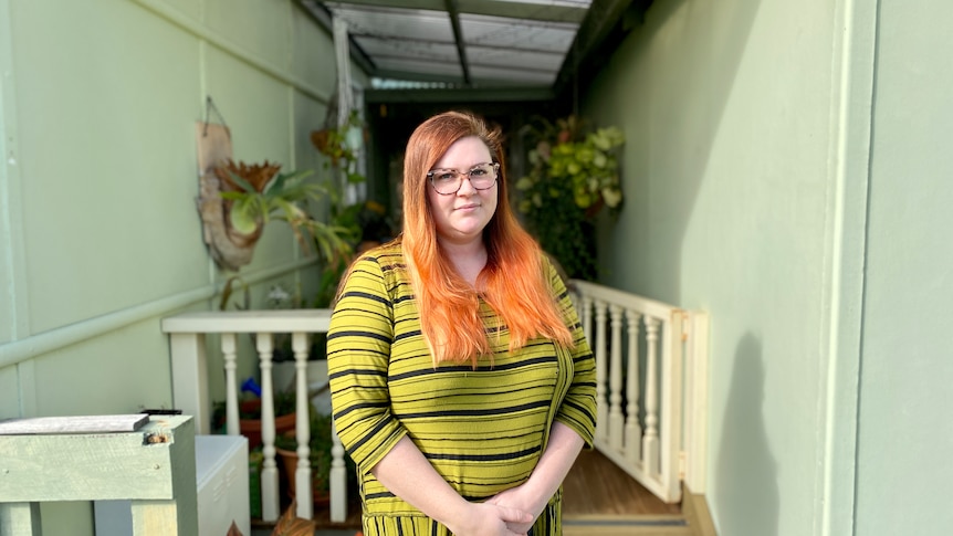 A woman with bright hair standing in front of her house.