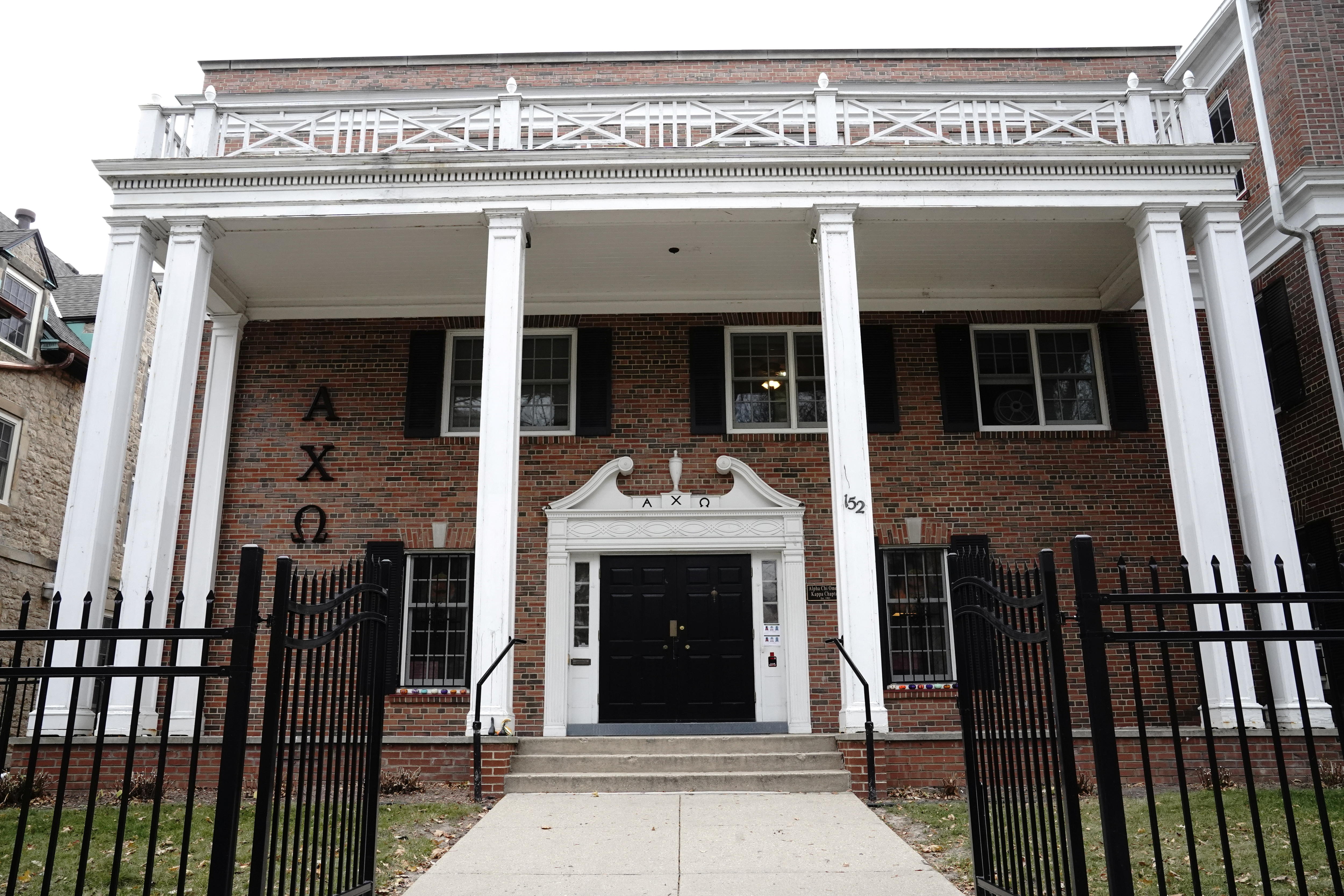 A house with large white pillars and a brick facade with greek letters written on the side.