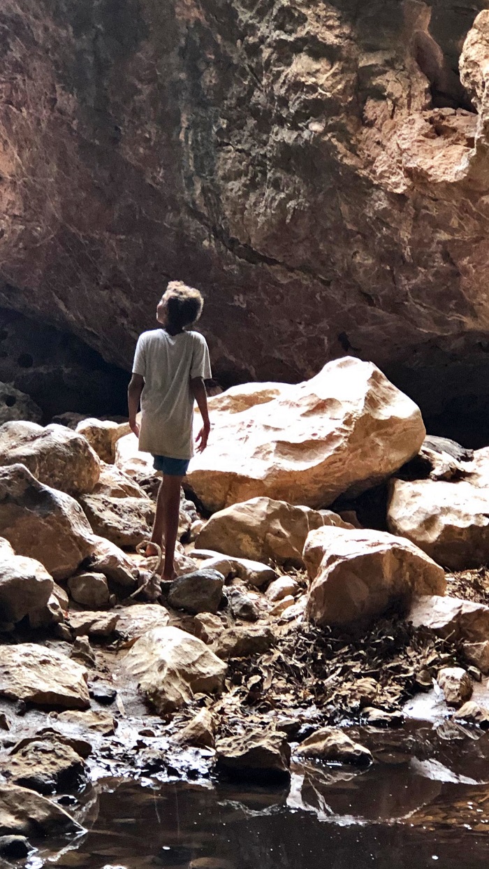 An Aboriginal boy looks up at red rock cliffs in soft light