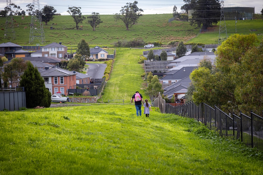 A man walking with a young girl on grass between houses