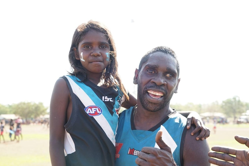 Mark Airuu gives the thumbs up while carrying an adoring fan in Wadeye.