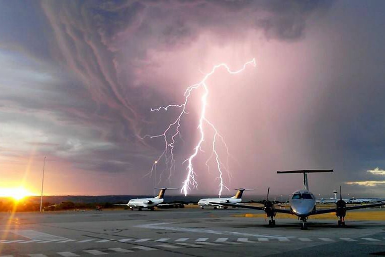 Lightning strike above two planes on the tarmac.