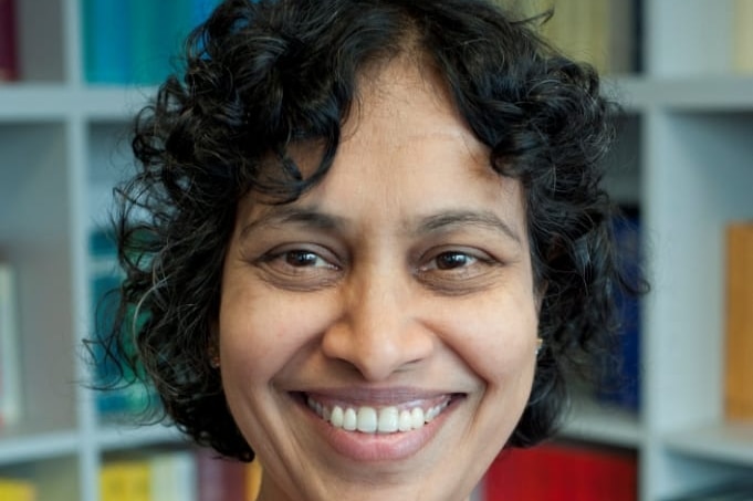 A smiling middle-aged woman of Indian origin wearing ethnic shift looks at camera in library.