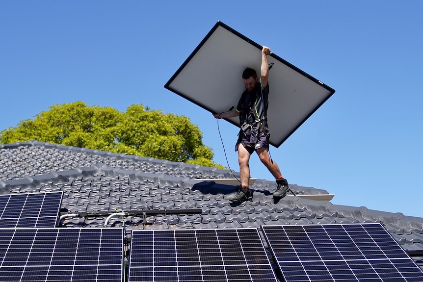 A man installs solar panels on the roof of a house.