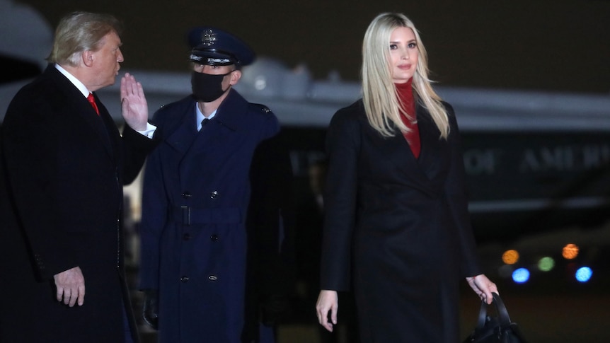 Donald Trump and Ivanka Trump walk past an Air Force One officer in the dark.