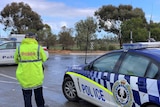 A police officer in a raincoat and a police car on a wet country road
