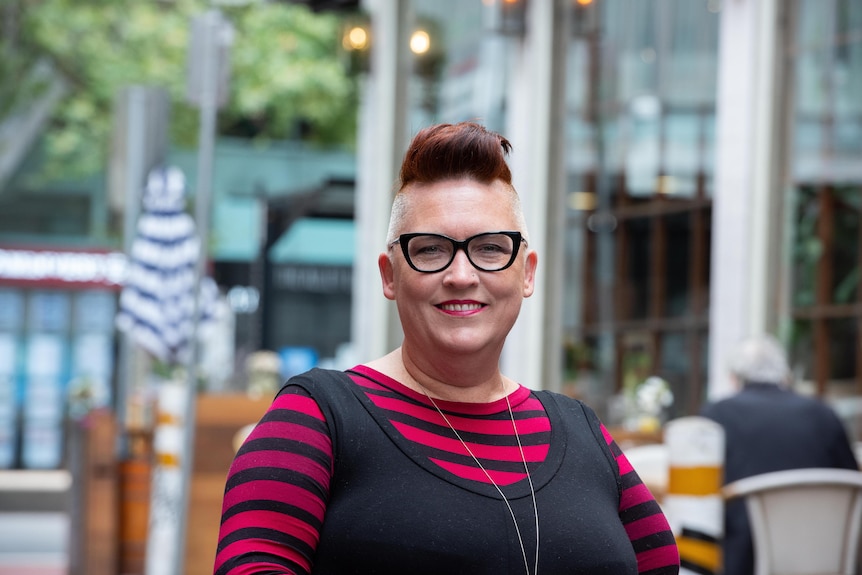 Amanda Kelly, wearing thick-rimmed black glasses and a striped top, smiles at the camera.