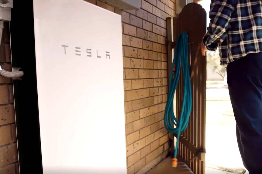 A Tesla battery attached to the outside of a home.