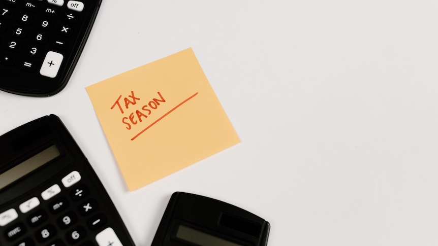 Three black calculators on a white table with a yellow post-it note that says 'tax season' in red marker