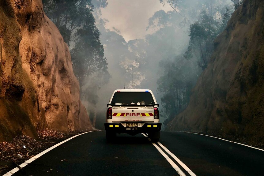 A fire truck driving up a smoky road.