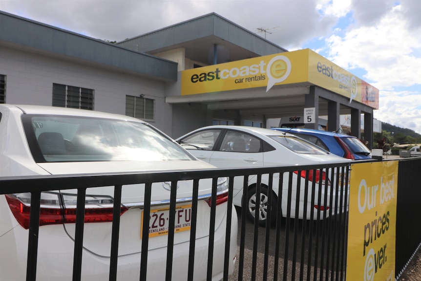 A row of cars parked behind a fence with signage for East Coast Car Rentals