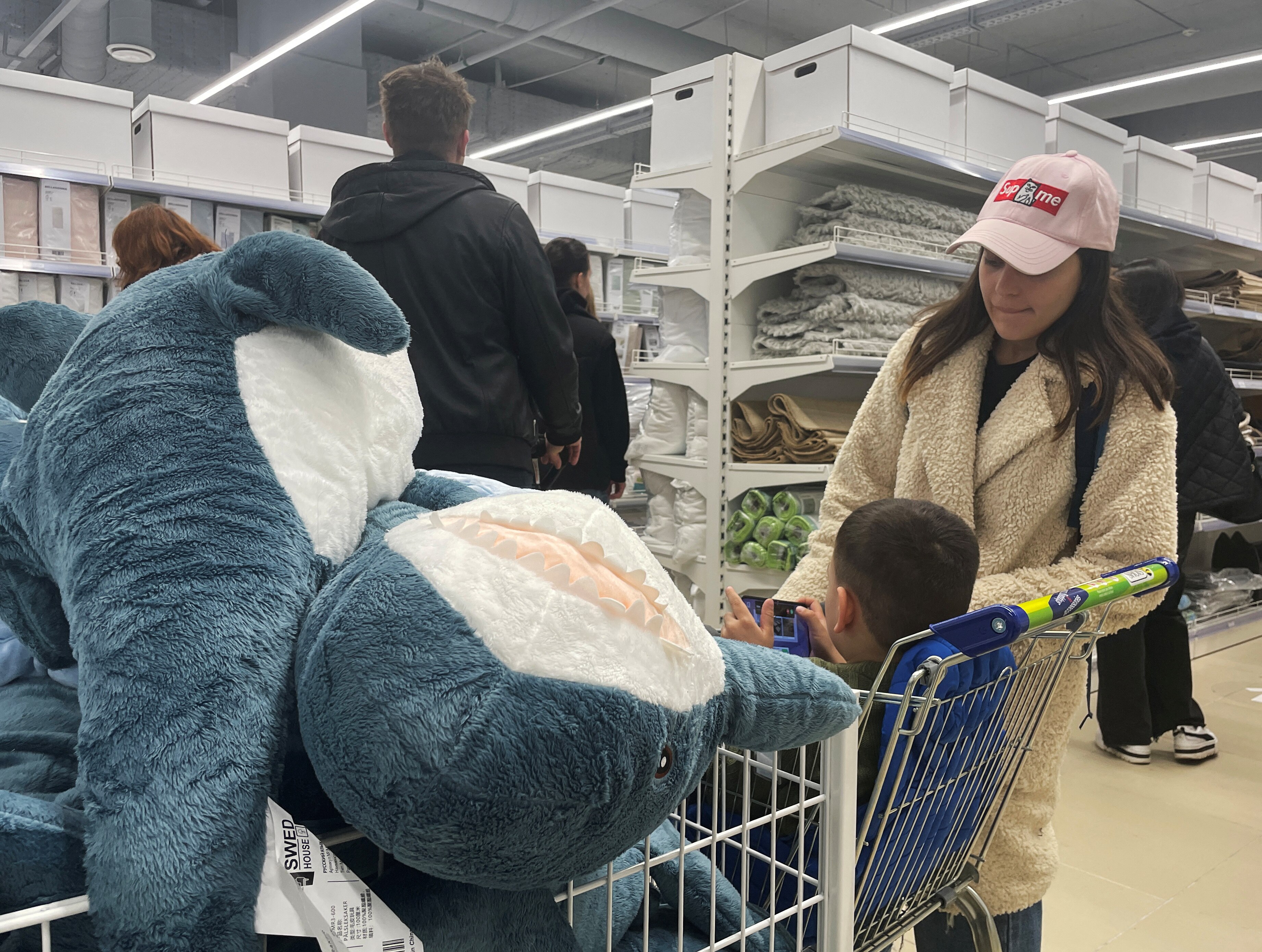 A woman and a boy look at fluffy toy sharks in a store.