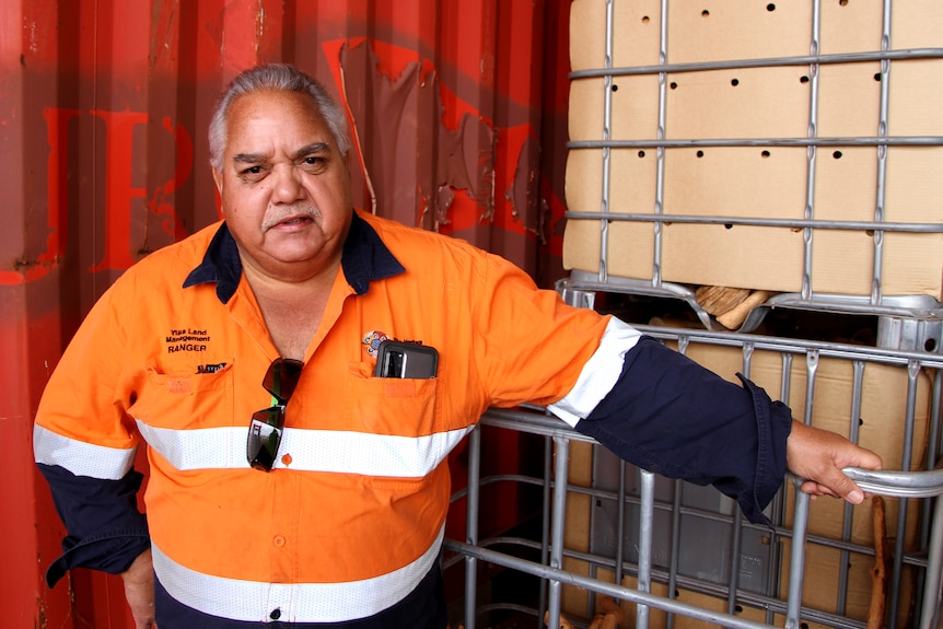 He wears hi-vis and leans on a crate of sandalwood