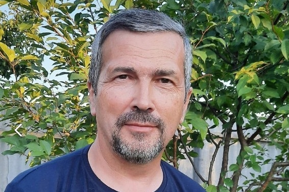 A man in a t-shirt smiles at the camera.