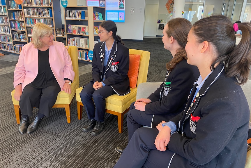 A woman in a pink blazer speaking to three school students.