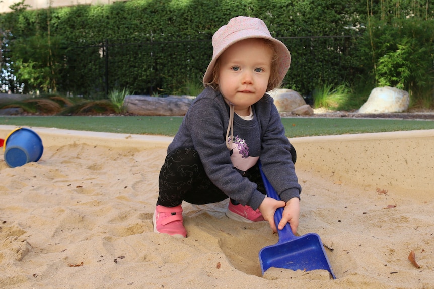 A child with a hat plays in a sandpit at a childcare centre playground.