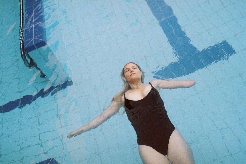 A woman is without an arm amputated is floating in a pool with her eyes closed