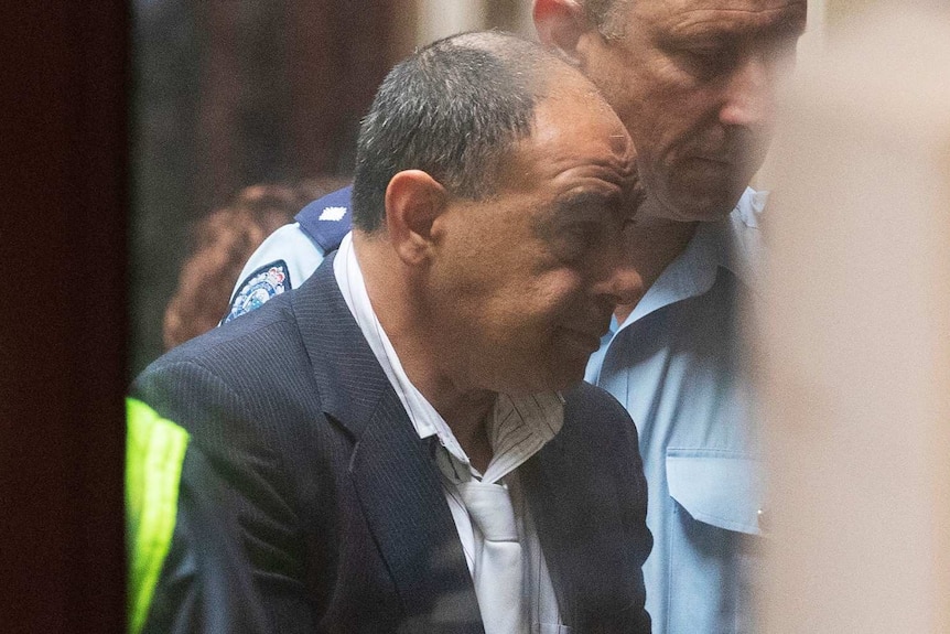 Murat Davsanoglu, wearing a suit jacket, is led into court.