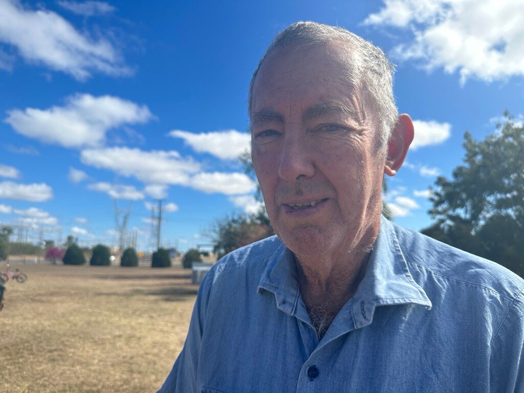 An older man stands outside beneath a sunny sky.