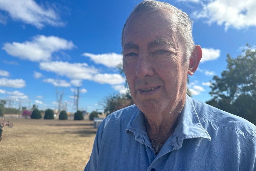 An older man stands outside beneath a sunny sky.