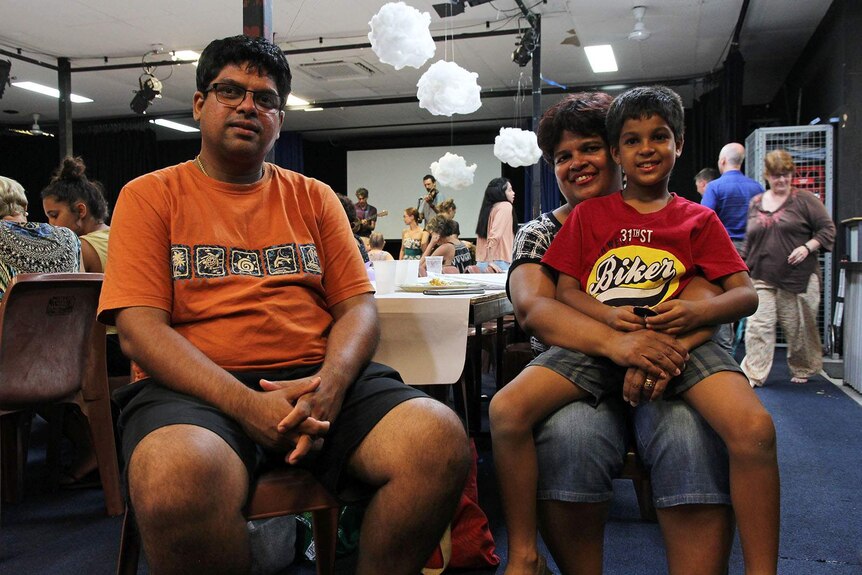 An Indian family sit on chairs in a community hall.