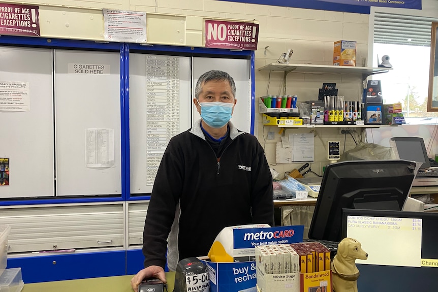 A man stands at a cash register with a cigarette cabinet behind him