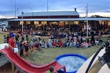 A large crowd sitting and standing around a ute and paddling pool full of water.