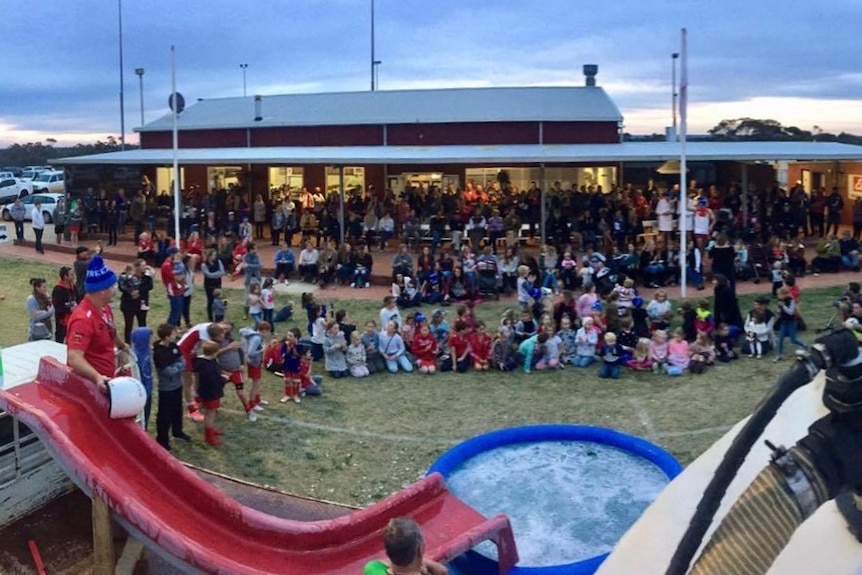 A large crowd sitting and standing around a ute and paddling pool full of water.