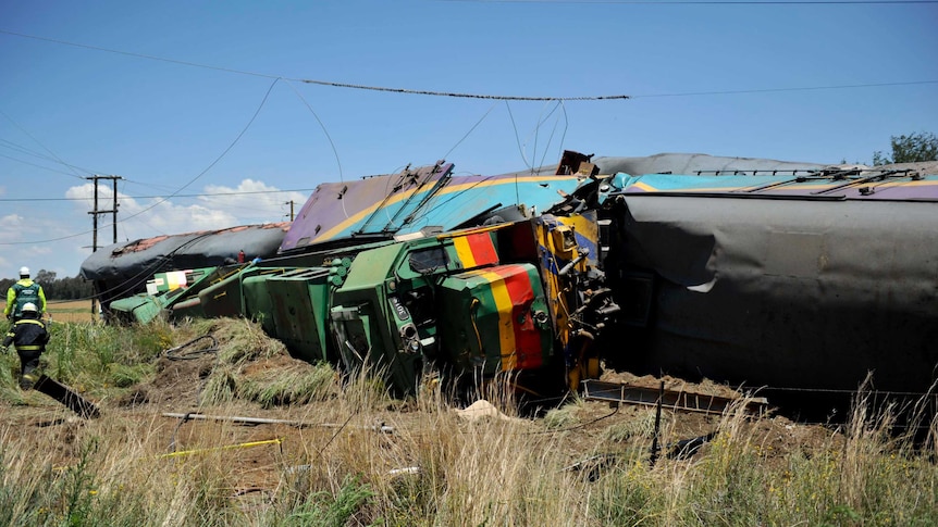A damaged train lies on its side in long grass.