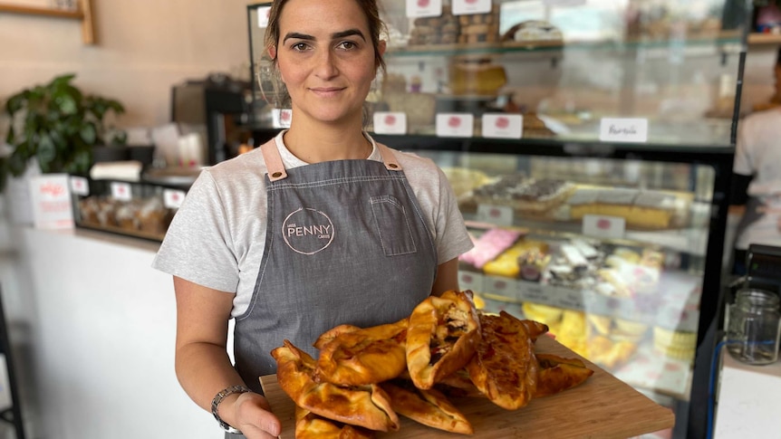 Penny Kerasiotis wearing an apron with her business's name and holding a wooden platter of pastries.