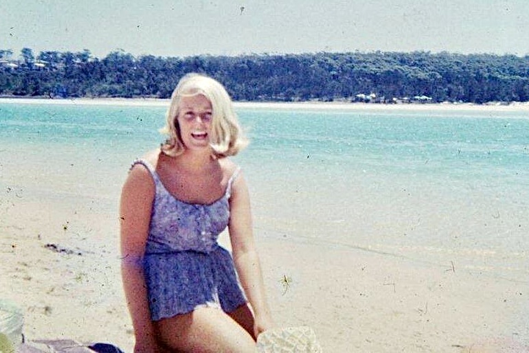 A woman sits by the beach on a blue-sky day 