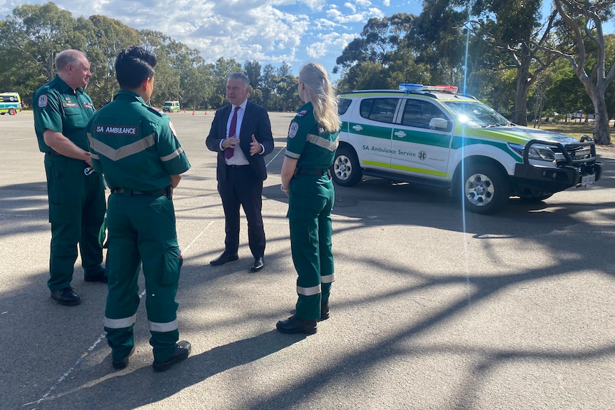 Health Minister Stephen Wade speaks with three paramedics with an ambulance vehicle in the background