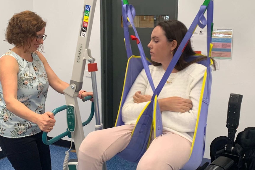 A young woman sits in a hoisted swing while another woman operates the controls.