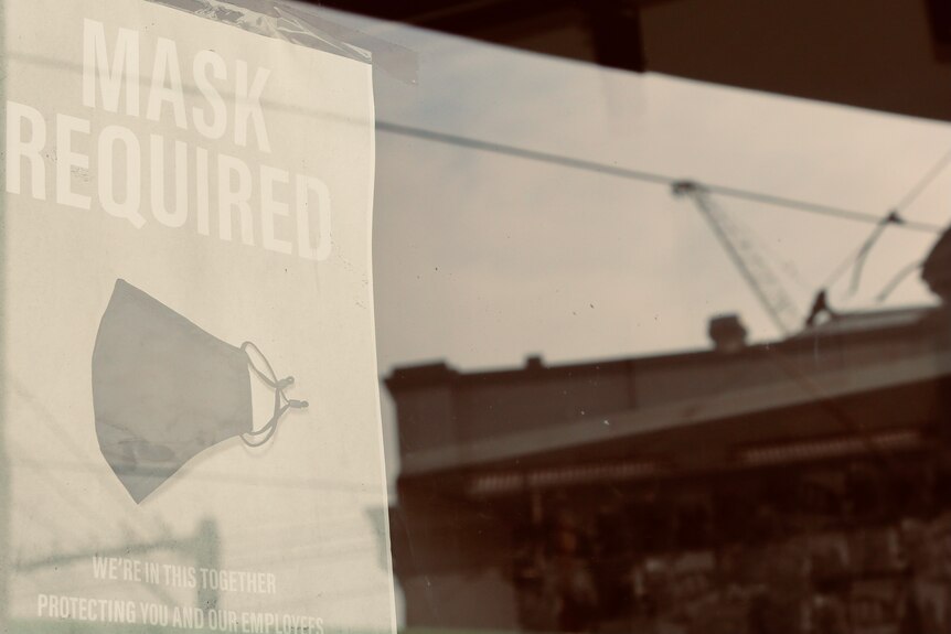 A business window with a sign about masks with the silhouette of a crane reflected.